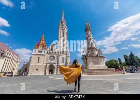 Il viaggiatore con il mantello giallo cammina verso la chiesa di Mattia e la colonna della Santissima Trinità a Budapest in una giornata di sole Foto Stock