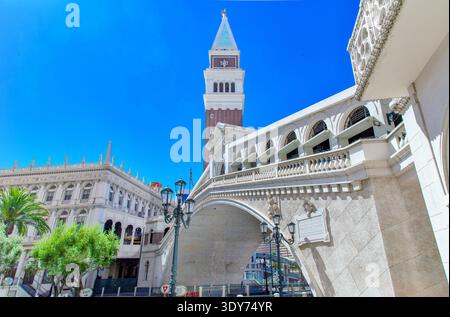 L'alta torre dell'orologio si erge sopra il ponte e gli edifici durante una giornata limpida in una città storica in Italia Foto Stock
