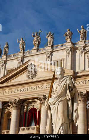 La statua di San Pietro si erge di fronte alla Basilica di San Pietro a Roma, con un cielo azzurro e un'architettura storica Foto Stock