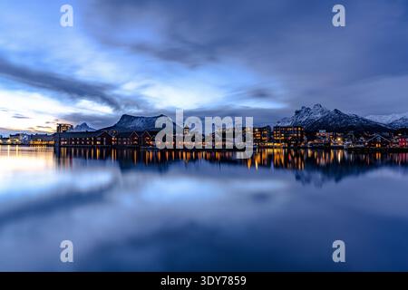 La luce serale risplende sui riflessi della città e delle montagne nel fiordo al crepuscolo nelle isole Lofoten in Norvegia Foto Stock