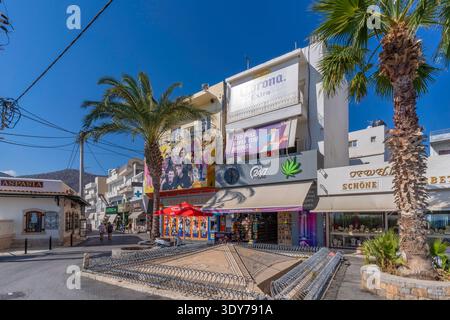 I negozi fiancheggiano una strada principale a Limenas Chersonisou con palme e cartelli luminosi a Creta Foto Stock