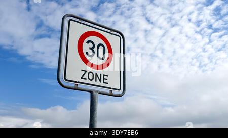 Segnale stradale che indica un limite di velocità di 30 zone su uno sfondo di cielo blu con nuvole sparse Foto Stock