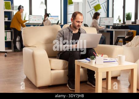 Uomo d'affari strart su ufficio moderno digitando sul laptop seduto sul divano cercando di terminare la scadenza importante progetto. Multietnico mixedraces successo collaboratori imprenditore lavorare insieme Foto Stock