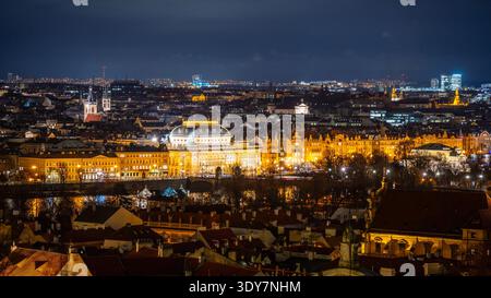 La scena mostra il Teatro Nazionale illuminato in modo luminoso contro il cielo notturno, con il panorama di Praga caratterizzato dai tetti e dalle luci della città sullo sfondo. Foto Stock