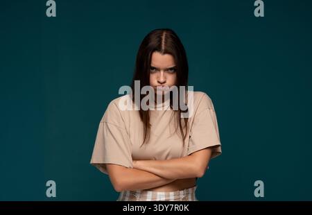 Una giovane donna arrabbiata che si mette a posare con le braccia incrociate, si sente frustrata e sconvolta su uno sfondo di tè minimale Foto Stock