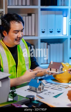 Ingegneri e architetti analizzano i modelli di costruzione e discutono le strategie di progetto, combinando conoscenze tecniche e idee creative per ottenere successo Foto Stock