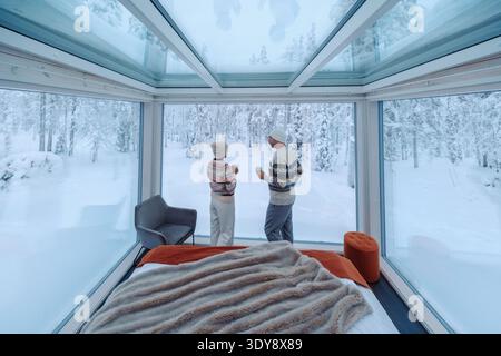 Due persone godono di viste mozzafiato da una lussuosa cabina di vetro ad Akaslompolo, Lapponia. Circondato da neve incontaminata, questo ambiente tranquillo invita rel Foto Stock