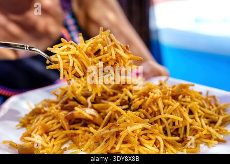 Piatto di spaghetti croccanti (spaghetti di ceci fritti) servito con una forchetta, spaghetti sottili dorati impilati sul piatto, fotografia di cibo ravvicinato Foto Stock