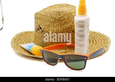 Cappello da sole in paglia con occhiali da sole e bottiglie di crema solare su sfondo bianco, indispensabili per viaggiare in estate Foto Stock