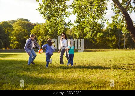 I bambini attivi e i loro genitori giocano a calcio nel parco, si muovono e ridono Foto Stock