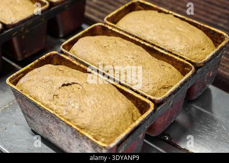 Impasto fermentato in padelle di pane pronto per la cottura presso la panetteria commerciale Foto Stock