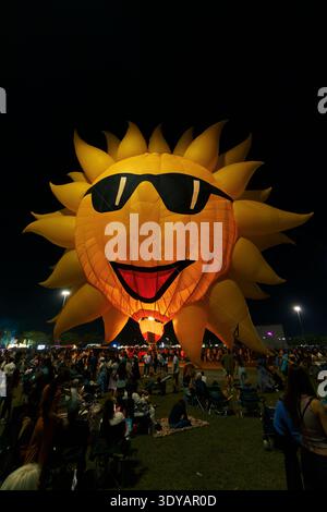 Durante il Miami Hot Air Balloon Festival al Tamiami Park, un gigante sorridente mongolfiera a forma di sole con occhiali da sole neri si illumina. Foto Stock