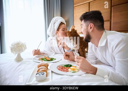 Coppia felice che si gusta la colazione con il cane in camera Foto Stock