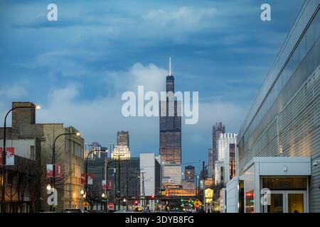 Il paesaggio urbano di Chicago al crepuscolo presenta la Willis Tower che si innalza sopra edifici urbani e lampioni sotto un cielo blu e nuvoloso Foto Stock