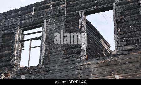 Rovine carbonizzate di una casa in legno bruciato con infissi vuoti di finestre contro un cielo coperto. Foto Stock