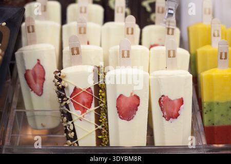 File di papaveri bianchi con fette di fragole incorporate e guarnizioni di noci di cioccolato in una vetrina refrigerata. Foto Stock