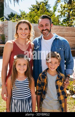 Ritratti, bambini e famiglia in giardino con un sorriso, unendosi e amore per il divertimento in natura. All'aperto, madre e padre con bambini, felicità per Foto Stock