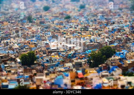 Ripresa aerea a turni di inclinazione di Jodhpur, la città blu dell'India, con tetti densamente pieni di blu, bianchi e gialli vivaci con alberi verdi sparsi Foto Stock