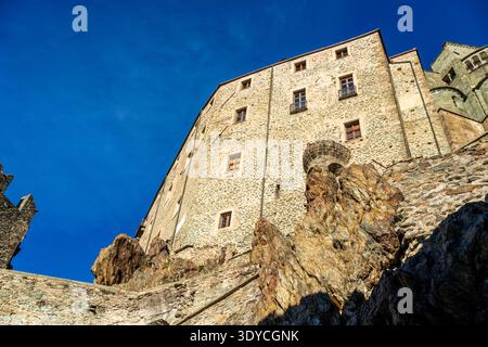 Vista ad angolo basso della Sacra di San Michele, simbolo del Piemonte. L'imponente facciata in pietra poggia direttamente sulla roccia grezza del Monte Pirchiriano, in piedi Foto Stock