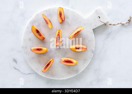 Un bordo rotondo di marmo sormontato da freschi segmenti di pesca maturi. Foto Stock