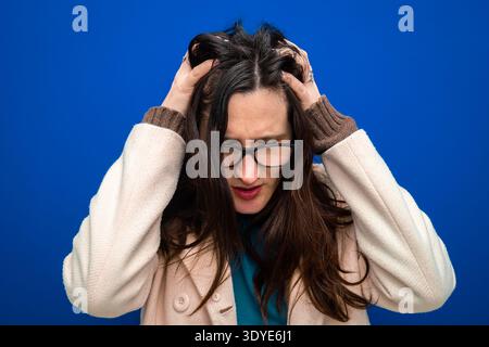 Donna stressata, ansiosa, con mal di testa, che tira i capelli con le mani sulla testa. Concetto di salute mentale Foto Stock