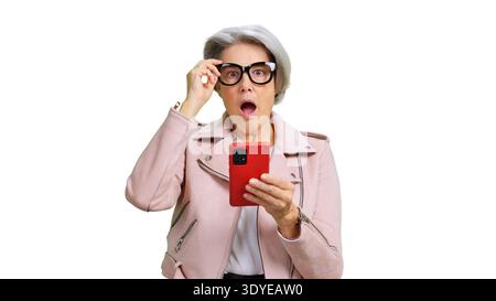 Donna anziana che reagisce con una sorpresa che tiene in mano lo smartphone rosso Foto Stock