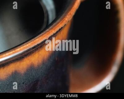 La tazza in ceramica calda si illumina di toni ambrati e marroni profondi. Lo smalto liscio rivela tratti di pennellate sottili e una texture artigianale. Gli interni scuri contrastano con Foto Stock