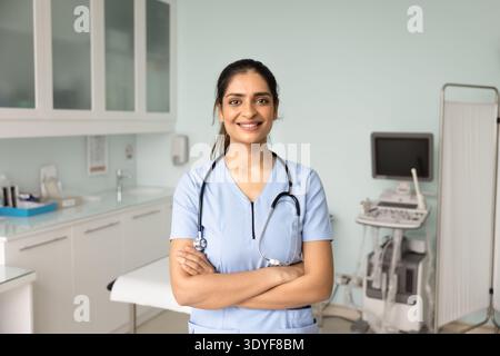 Giovane dottoressa sicura di sé in scrub blu in piedi in clinica Foto Stock