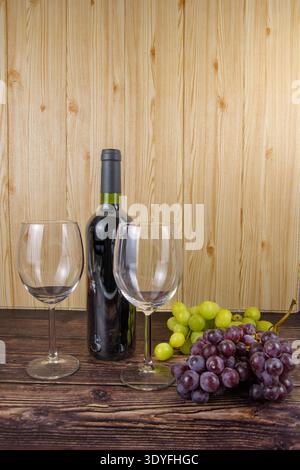 Bottiglia di vino con due bicchieri vuoti, uva verde e uva rossa su un rustico tavolo di legno, natura morta calda per la degustazione, ospitalità e abitudine al vigneto Foto Stock