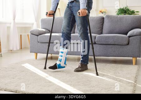 Foto ravvicinata di un uomo disabile con una gamba rotta che cerca di camminare usando le stampelle a casa Foto Stock