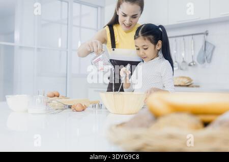 Mamma e figlia preparano biscotti insieme usando impasto e taglierine in cucina Foto Stock