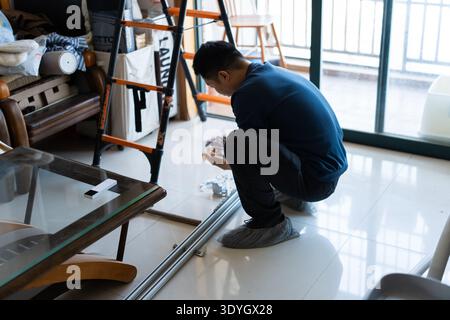 Uomo che installa una pista scorrevole per porte in vetro in interni moderni, Shanghai, Cina Foto Stock