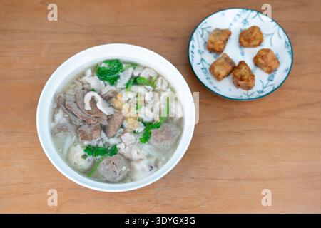 Zuppa di maiale in stile cantonese con gnocchi e tofu fritto servita su un tavolo di legno a Hong Kong Foto Stock
