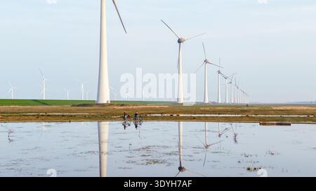 Due ciclisti si godranno un giro vicino alle turbine eoliche che si riflettono nel terremoto, mostrando la natura e l'energia rinnovabile. Un paio su una bicicletta elettrica A. Foto Stock