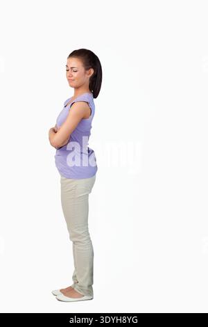 Donna in piedi di profilo in studio, rivolta a sinistra con le braccia incrociate, con top lilla, spazio copia. Ritratto, vista laterale, sereno, minimalista, abbigliamento casual, Foto Stock