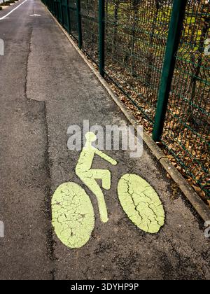 Simbolo verde della bicicletta intemprato dipinto su una pista ciclabile in asfalto che corre lungo una recinzione a rete metallica verde. Francia Foto Stock