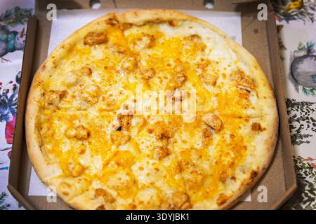 Pizza di pollo intera appena sfornata con formaggio fuso in una scatola di cartone. Foto Stock