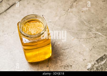 un vaso di vetro riempito di miele di tiglio dorato e favo su una superficie ruvida con luce naturale Foto Stock