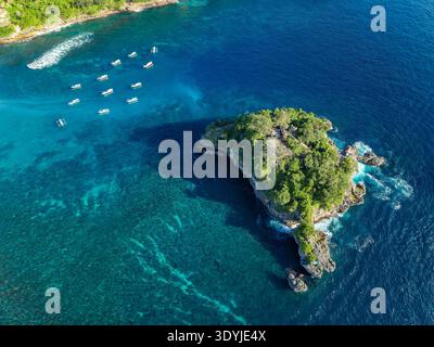 Veduta aerea con droni del lussureggiante isolotto roccioso e delle barche tradizionali a Crystal Bay, Nusa Penida Foto Stock