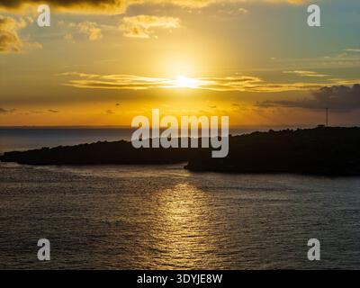 Incredibile tramonto di un'ora d'oro su una baia sull'oceano con una silhouette costiera scura e riflessi Foto Stock