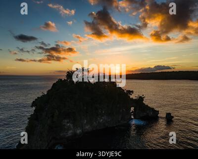 Vista aerea dell'isolotto roccioso che si staglia contro il tramonto dorato a Crystal Bay, Bali Foto Stock