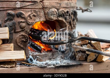 I tronchi di legna da ardere ardenti di fiamme e brace all'interno di un vecchio forno tradizionale in argilla, creando una calda atmosfera rustica Foto Stock