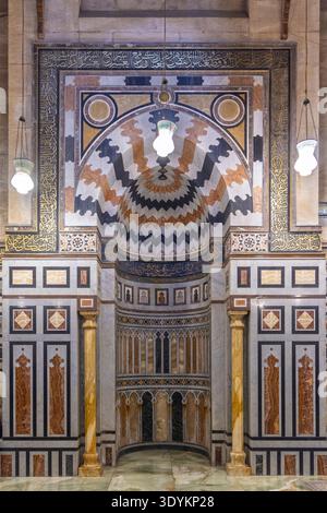 Elaborato mihrab islamico e interni decorati della moschea con intarsi in marmo, calligrafia araba e lampade a sospensione nella storica città del Cairo, in Egitto, showcasi Foto Stock