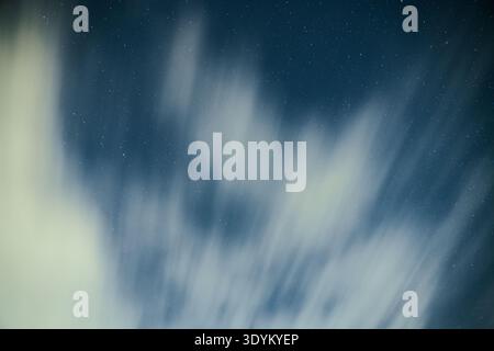 Cielo notturno a lunga esposizione con nuvole alla deriva che formano morbide piste di movimento su uno sfondo blu intenso pieno di stelle lontane, creando un An da sogno Foto Stock
