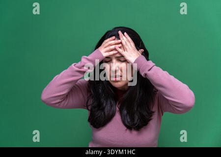 Donna che sente dolore intenso per mal di testa, che mette entrambe le mani sulla fronte, esprimendo disagio e frustrazione Foto Stock