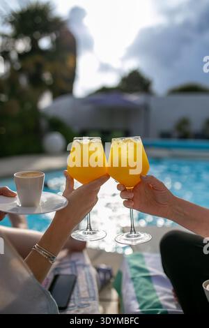 Cocktail Mimosa tenuti a bordo piscina, un classico brunch a base di spumante e succo d'arancia, per una festosa vacanza a bordo piscina Foto Stock