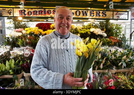 Ritratto di Ronnie, il proprietario di Ronnie's Flowers, in piedi presso la sua storica bancarella di fiori a Berwick Street Market, Soho, Londra. Foto Stock