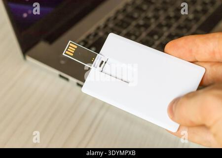 Una sottile scheda di memoria USB bianca inserita nello slot USB laterale di un computer laptop su un tavolo di legno chiaro. Foto Stock