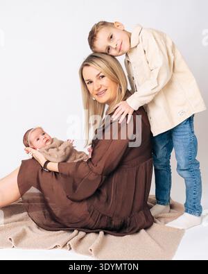 Madre seduta con i suoi figli neonato e figlio maggiore. Caldo ritratto di famiglia che mostra maternità, amore e forte legame emotivo tra Foto Stock