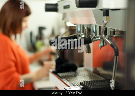Primo piano delle mani del barista che utilizzano una macchina per caffè espresso professionale per preparare bevande a base di caffè in un ambiente moderno. Foto Stock